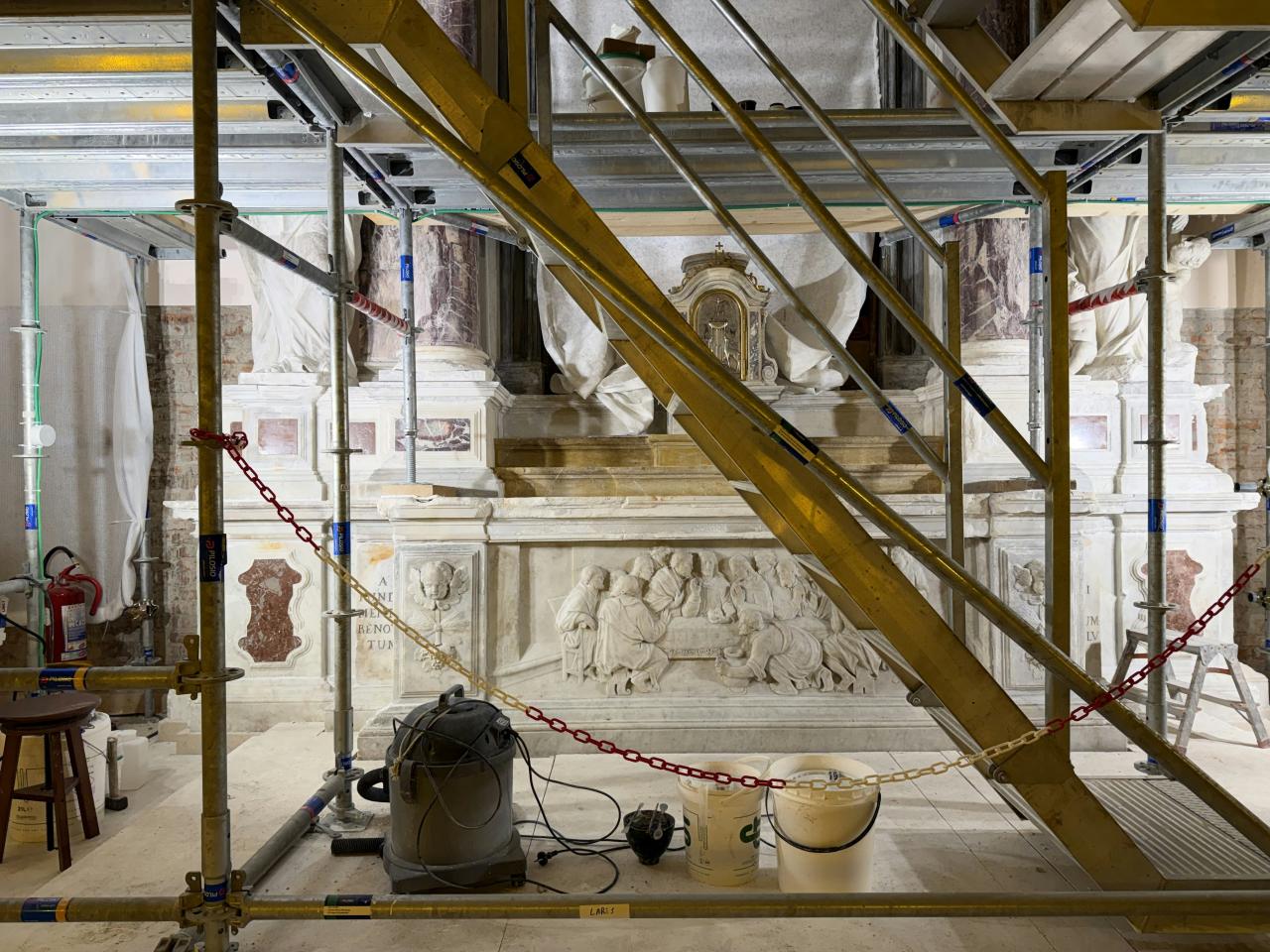 Scaffolding surrounds ornate marble tomb with relief carvings.
